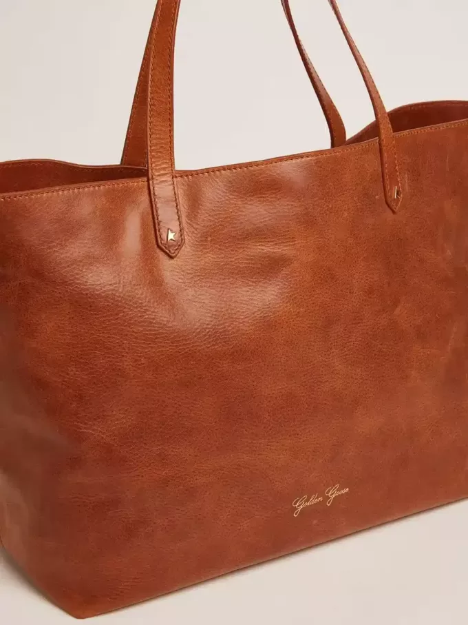 Pasadena-Tasche aus hellbraunem, glänzendem, gehämmertem Leder mit goldenem Logo auf der Vorderseite Pasadena-Tasche aus hellbraunem, glänzendem, gehämmertem Leder mit goldenem Logo auf der Vorderseite