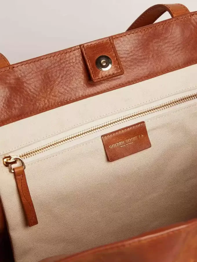 Pasadena-Tasche aus hellbraunem, glänzendem, gehämmertem Leder mit goldenem Logo auf der Vorderseite Pasadena-Tasche aus hellbraunem, glänzendem, gehämmertem Leder mit goldenem Logo auf der Vorderseite